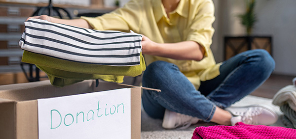 Smiling contented volunteer sitting on the floor and placing pieces of clothing into the carton